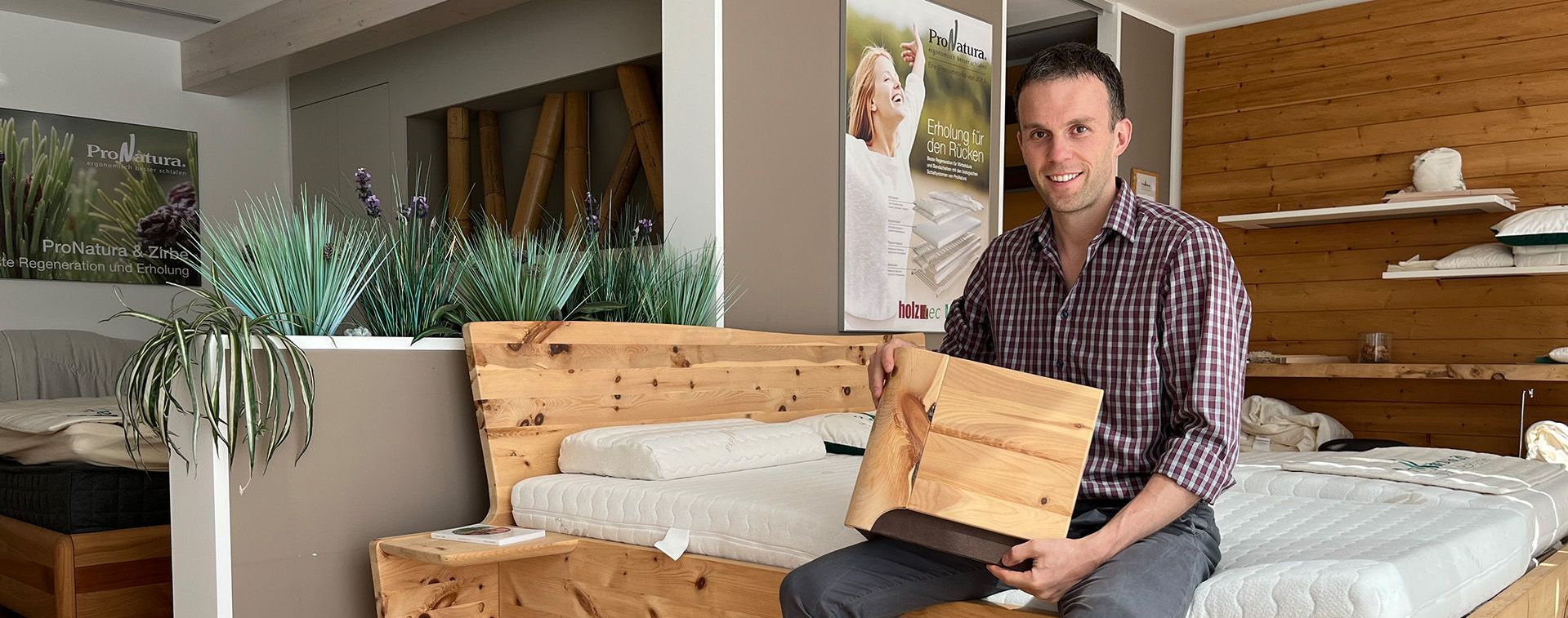Christian Schleupen sitzt auf Bett in Ausstellung und hält ein Muster in der Hand