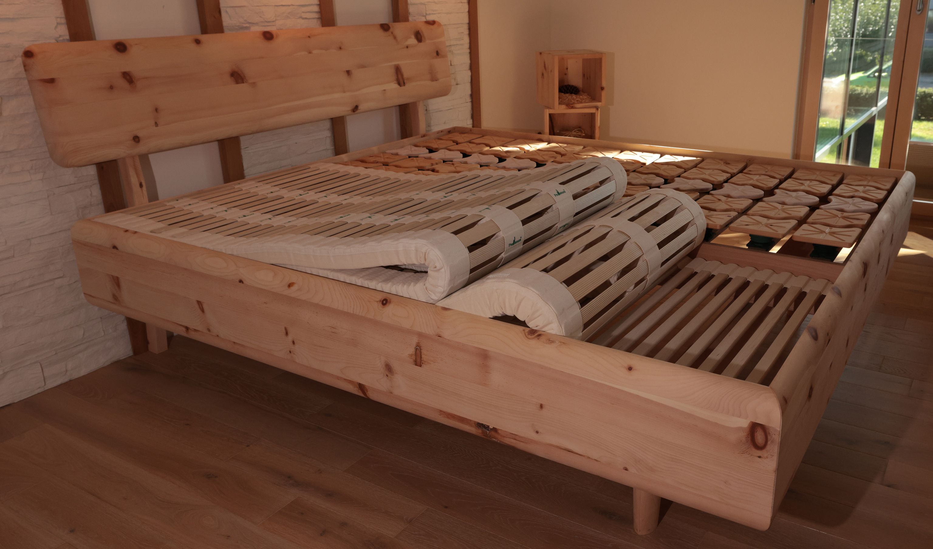 Zirben Doppelbett, auf der Linken Liegefläche ist ein Lamellenrost, welches zum Zeigen halb aufgerollt ist. Auf der Rechten Liegefläche ist ein Tellersystem. 