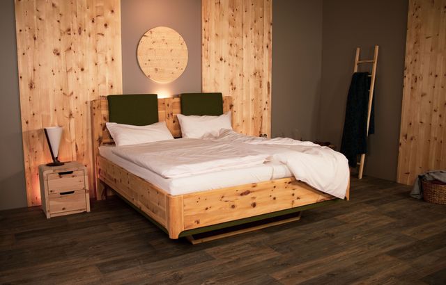 Zirbenbett mit Grünen Akzentleisten und zwei Grünen Polstern. Die Ecke am Fußteil sind stark gerundet. Ein Nachtisch mit zwei Schubladen. 