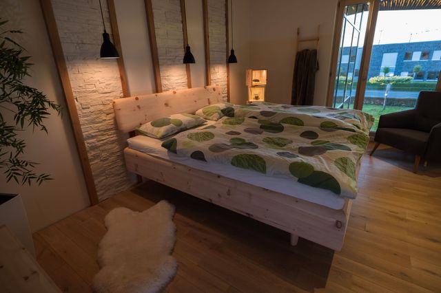 Doppelbett in Zirbe, mit auf Gehrung gearbeiteten Ecken. Grüngepunktete Decke. 