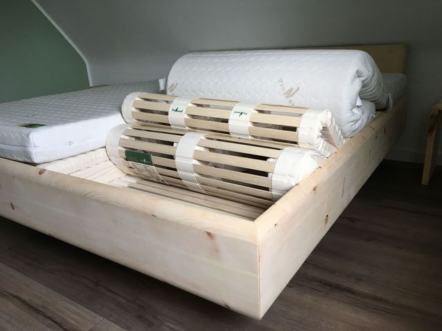 Detail vom Fußteil des Bettes, es ist auf Gehrung gearbeitet. Das Schlafsystem und die Matratze sind halb aufgerollt. 